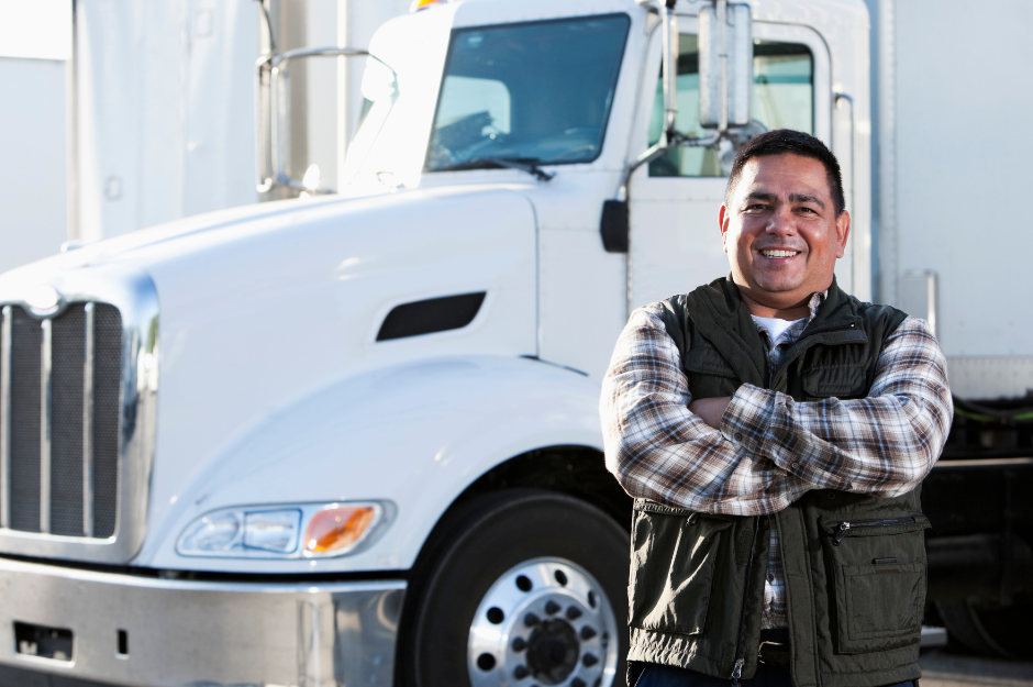 A man is standing in front of a white semi truck with his arms crossed.