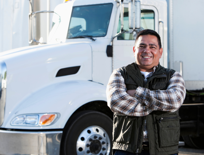 A man is standing in front of a white semi truck with his arms crossed.