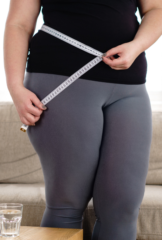 A woman is measuring her waist with a tape measure