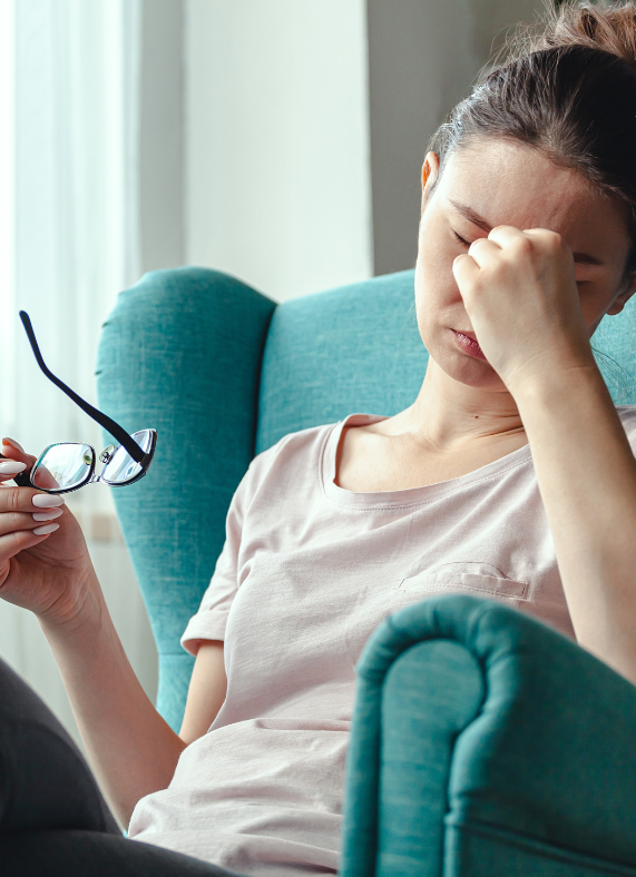 A woman is sitting in a chair with her hand on her forehead.