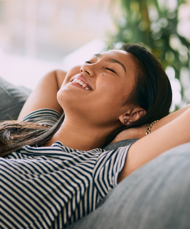 A woman is laying on a couch with her eyes closed and smiling.