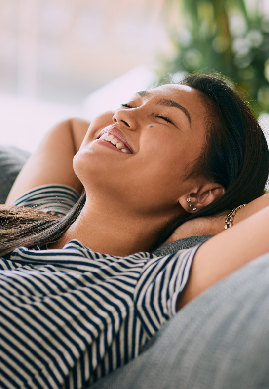 A woman is laying on a couch with her eyes closed and smiling.