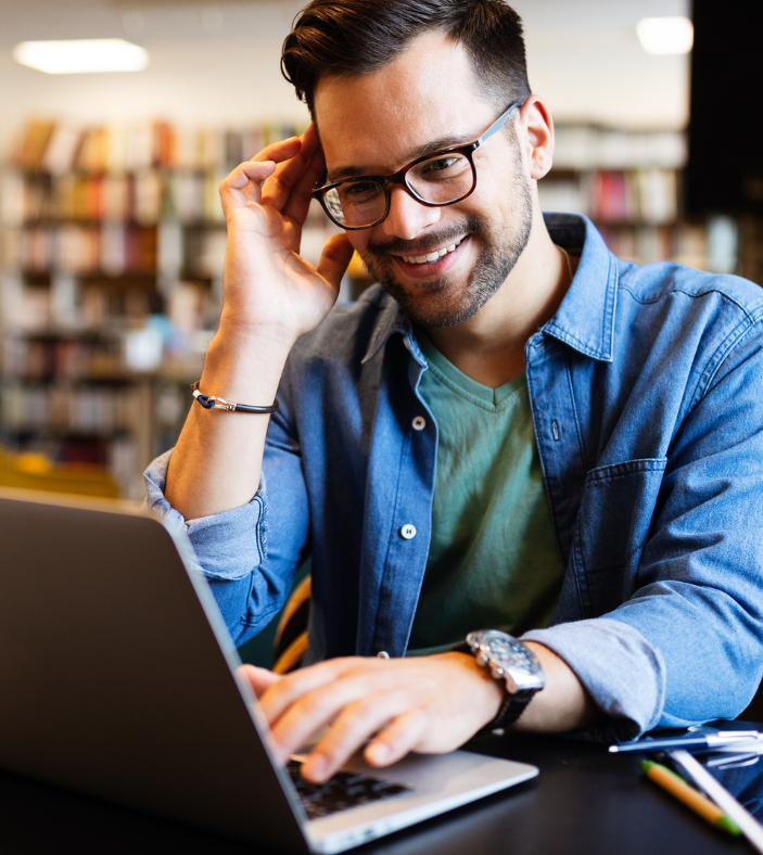 A man wearing glasses is typing on a laptop computer