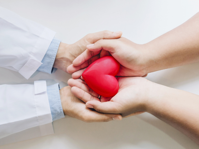 A doctor and a patient are holding a red heart in their hands.