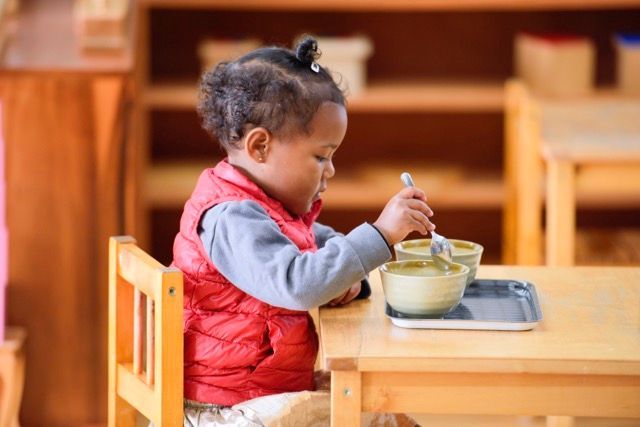 Child sorting objects in a bowl at a table in a classroom