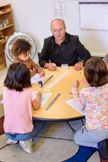 Two adults and three children sitting around a round table doing a classroom activity