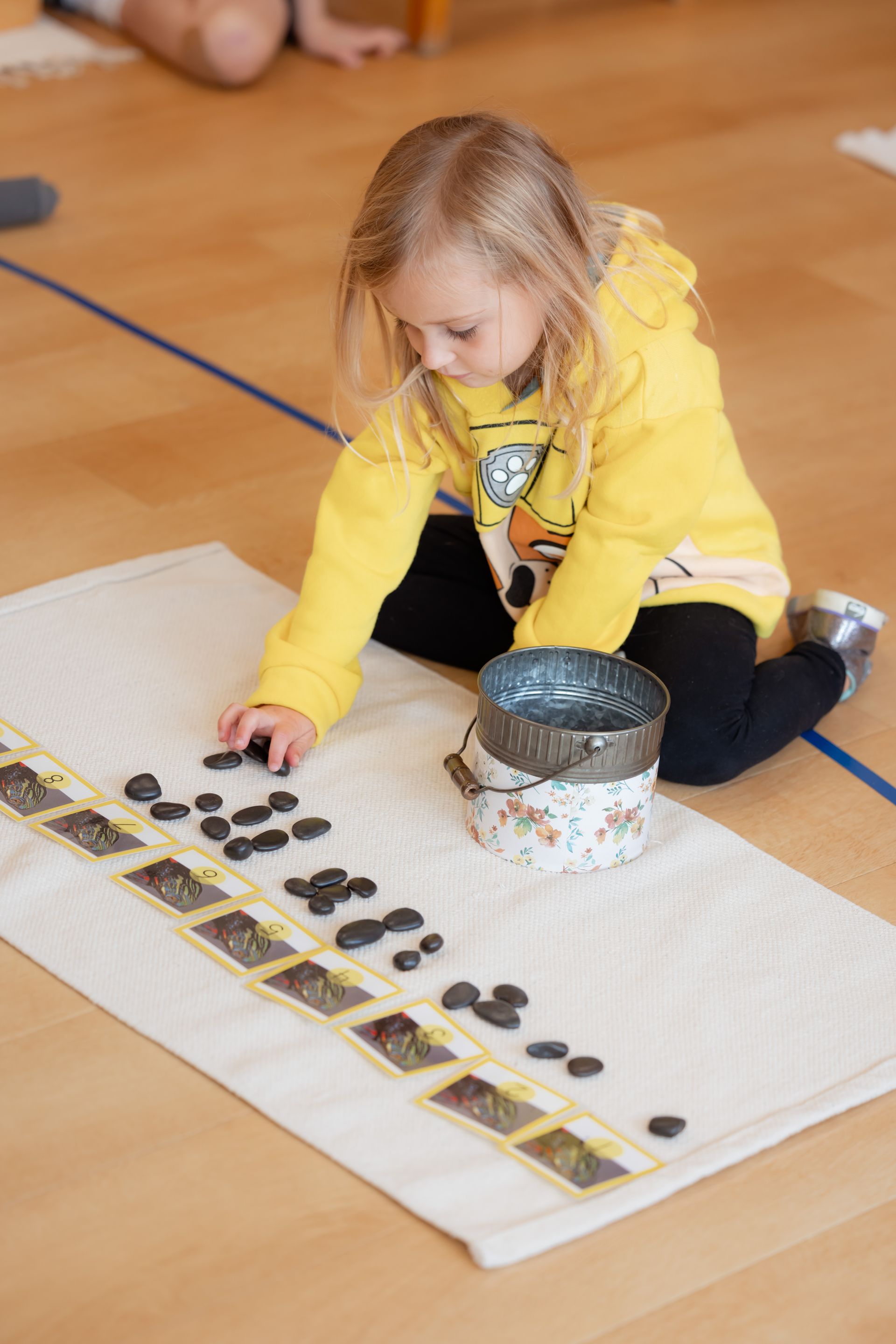 Child in a yellow jacket working with the cards and counters on a mat indoors