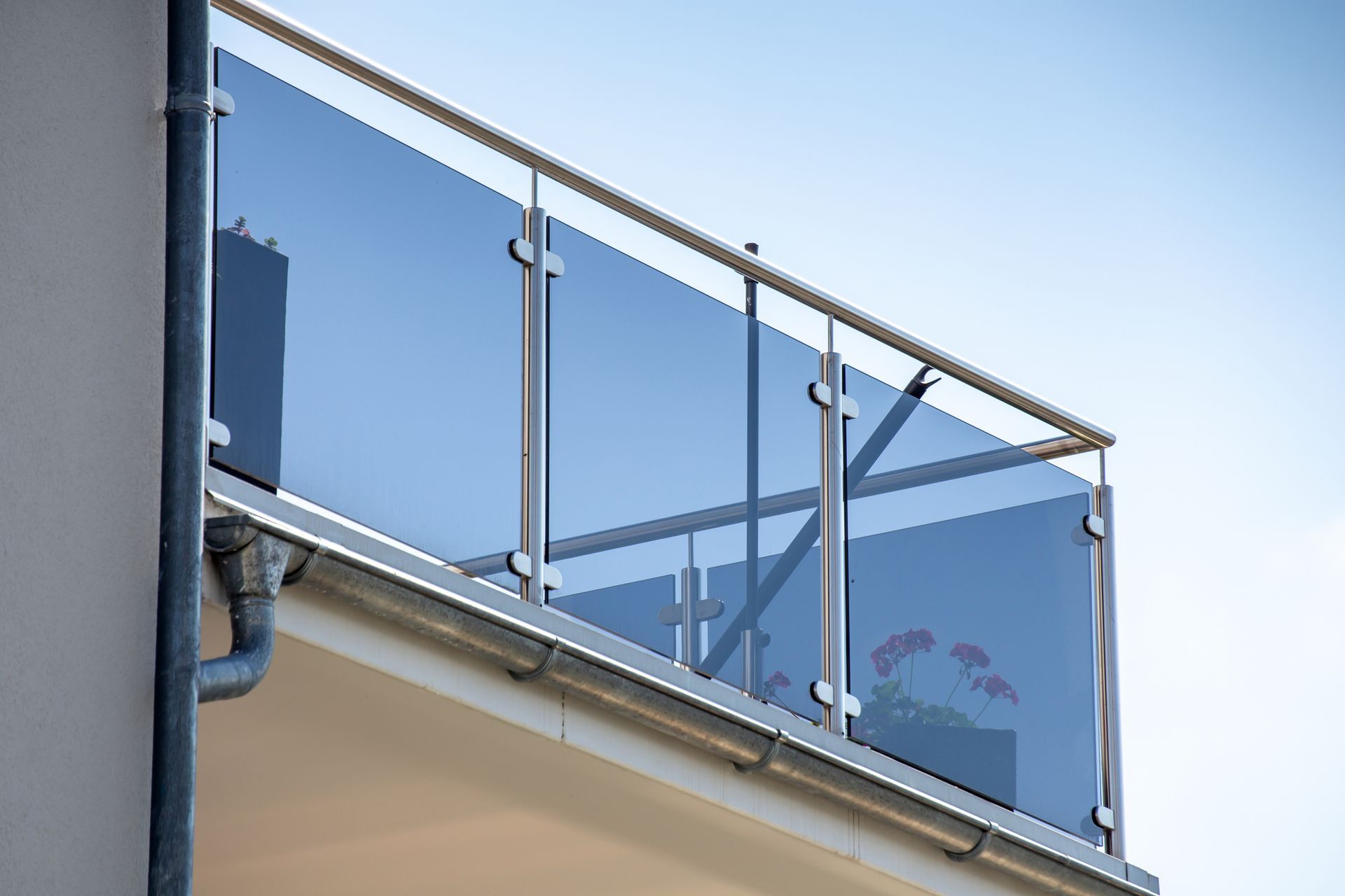 Balcony with glass panels and a metal railing against a blue sky. A portion of a building's side is visible on the left.