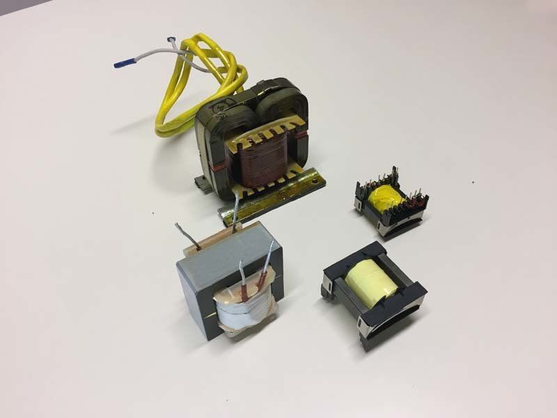 Quattro trasformatori elettrici di diverse dimensioni e forme sono posizionati su una superficie bianca.