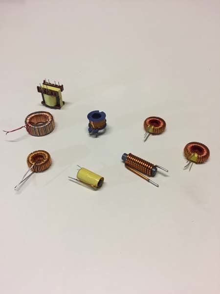 Vari induttori e trasformatori elettronici su una superficie bianca, con bobine di filo di rame, condensatori gialli e varie disposizioni dei pin.