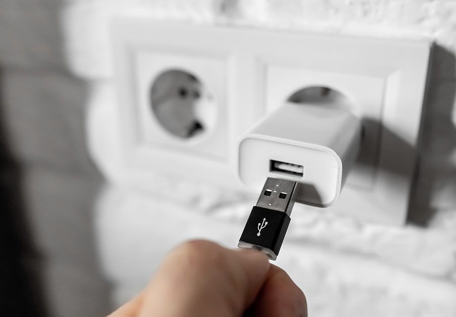 Mano che inserisce un cavo USB in un caricabatterie bianco per telefono collegato a una presa a muro.