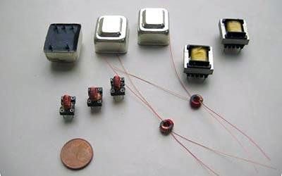 Componenti elettronici di varie dimensioni, tra cui trasformatori, accanto a una moneta da un centesimo.