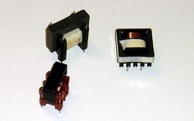 Tre piccoli trasformatori di diverse dimensioni e colori, nero e rosso, con avvolgimenti in rame visibili.