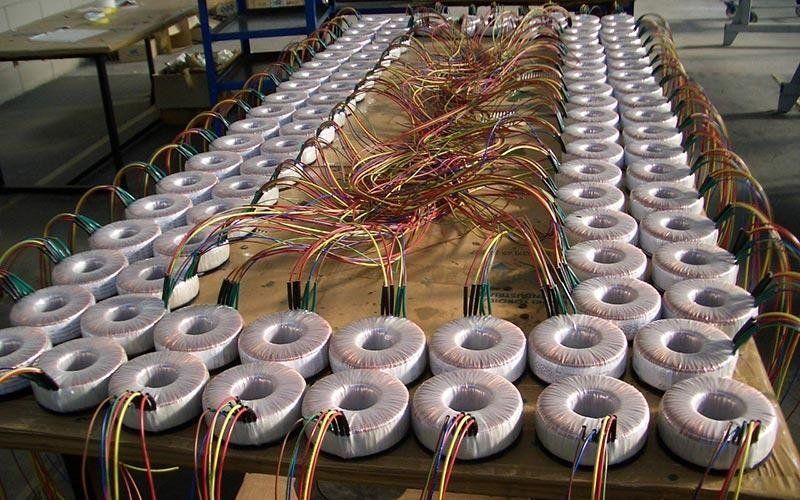 File di trasformatori elettrici con fili multicolori su un tavolo di legno.
