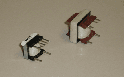 Due piccoli trasformatori elettrici, bianchi, con elementi marroni e neri, su una superficie neutra.