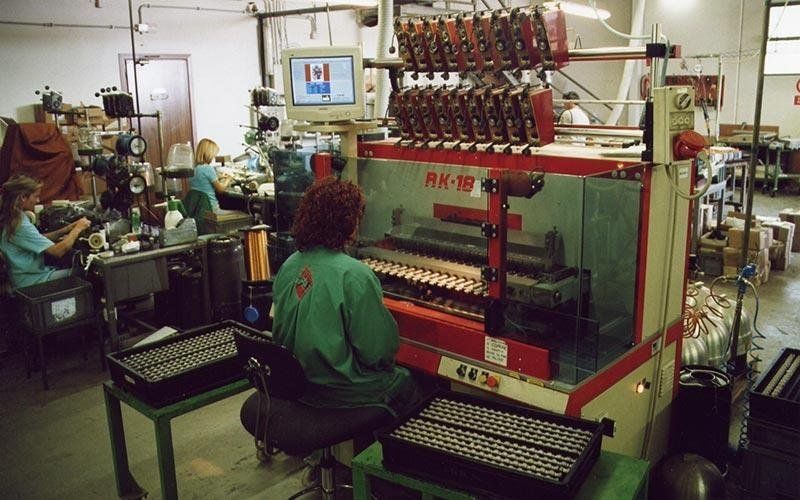 Gli operai di una fabbrica azionano i macchinari. Uno è concentrato su una macchina rossa, gli altri lavorano alle postazioni. Ambientazione interna.