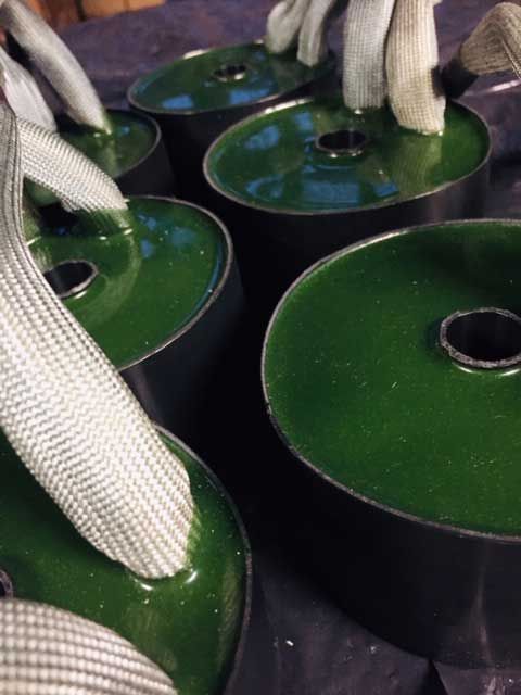 Cilindri metallici dipinti di verde, probabilmente parti di macchine, tenuti insieme da cinghie bianche.