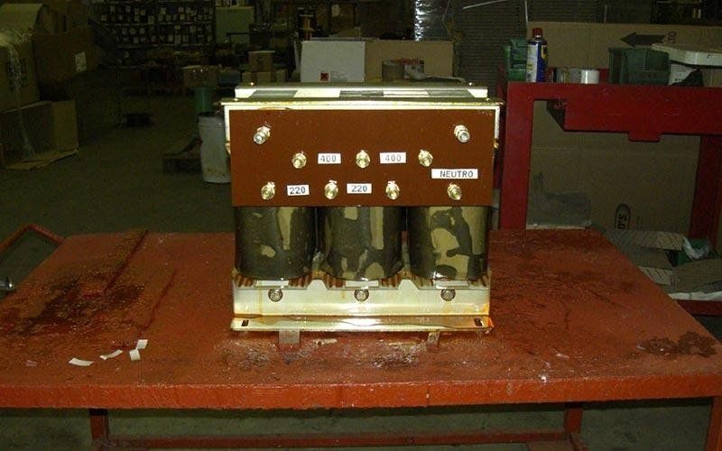 Trasformatore trifase con bobine marroni e mimetiche su un tavolo rosso in una fabbrica.