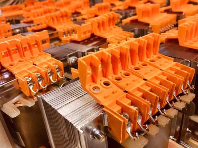 Connettori elettrici arancioni sopra un componente metallico, probabilmente per l'assemblaggio della batteria.