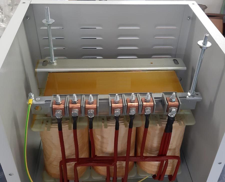 Contenitore aperto contenente componenti di trasformatori elettrici. Terminali in rame, fili marroni, alloggiamento metallico.