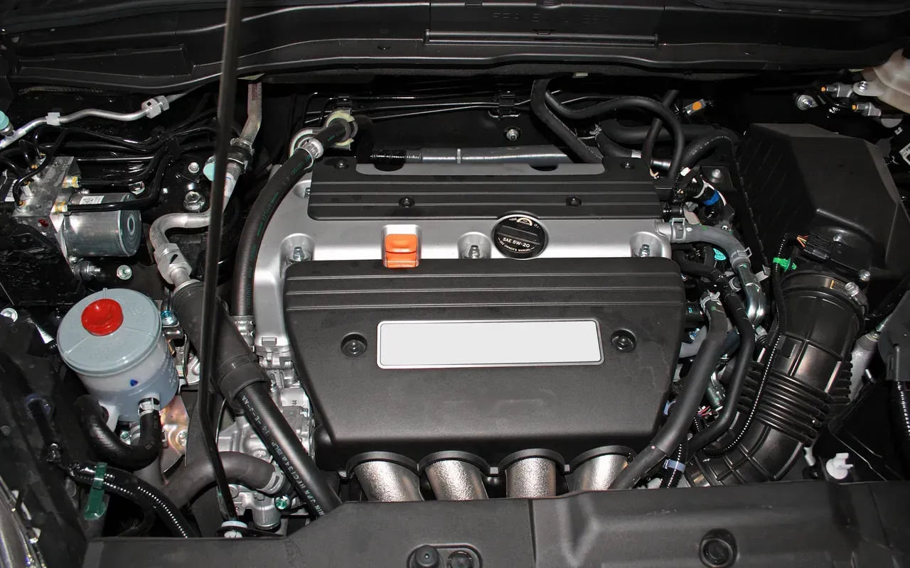 Car engine bay with a black cover, silver intake tube, and visible fluid reservoirs under the hood