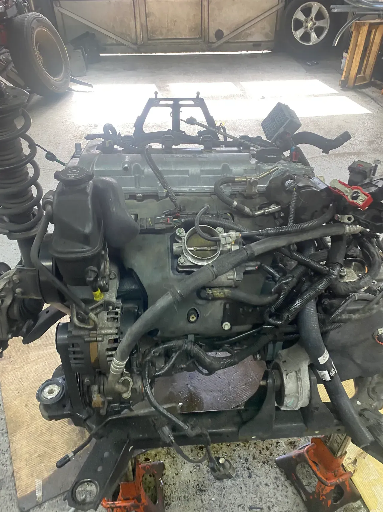 Engine mounted on a wheeled stand in a workshop, with hoses and wiring exposed.