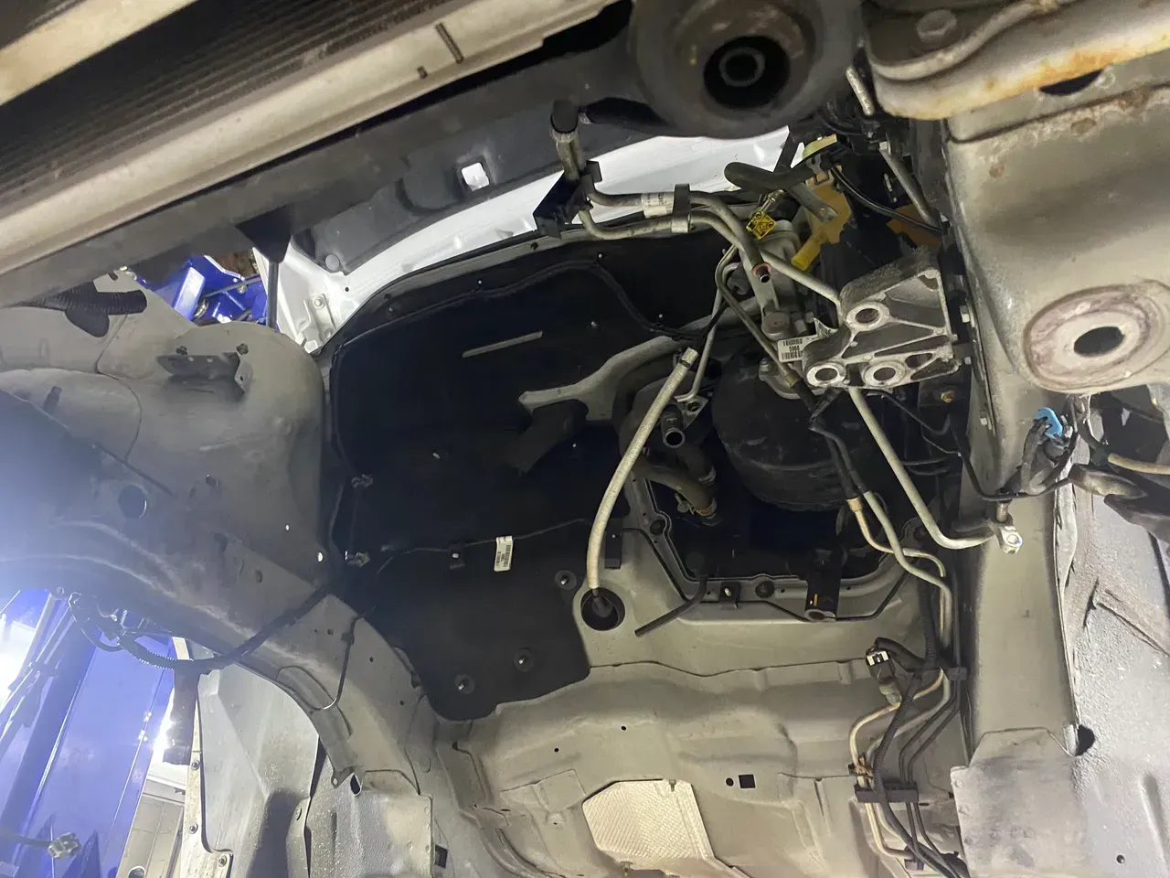 Exposed vehicle undercarriage with wiring, metal frame, and detached interior panels in a repair area