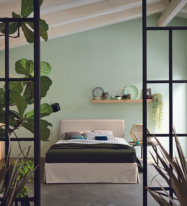 Camera da letto con letto, parete verde, piante e struttura in metallo nero.