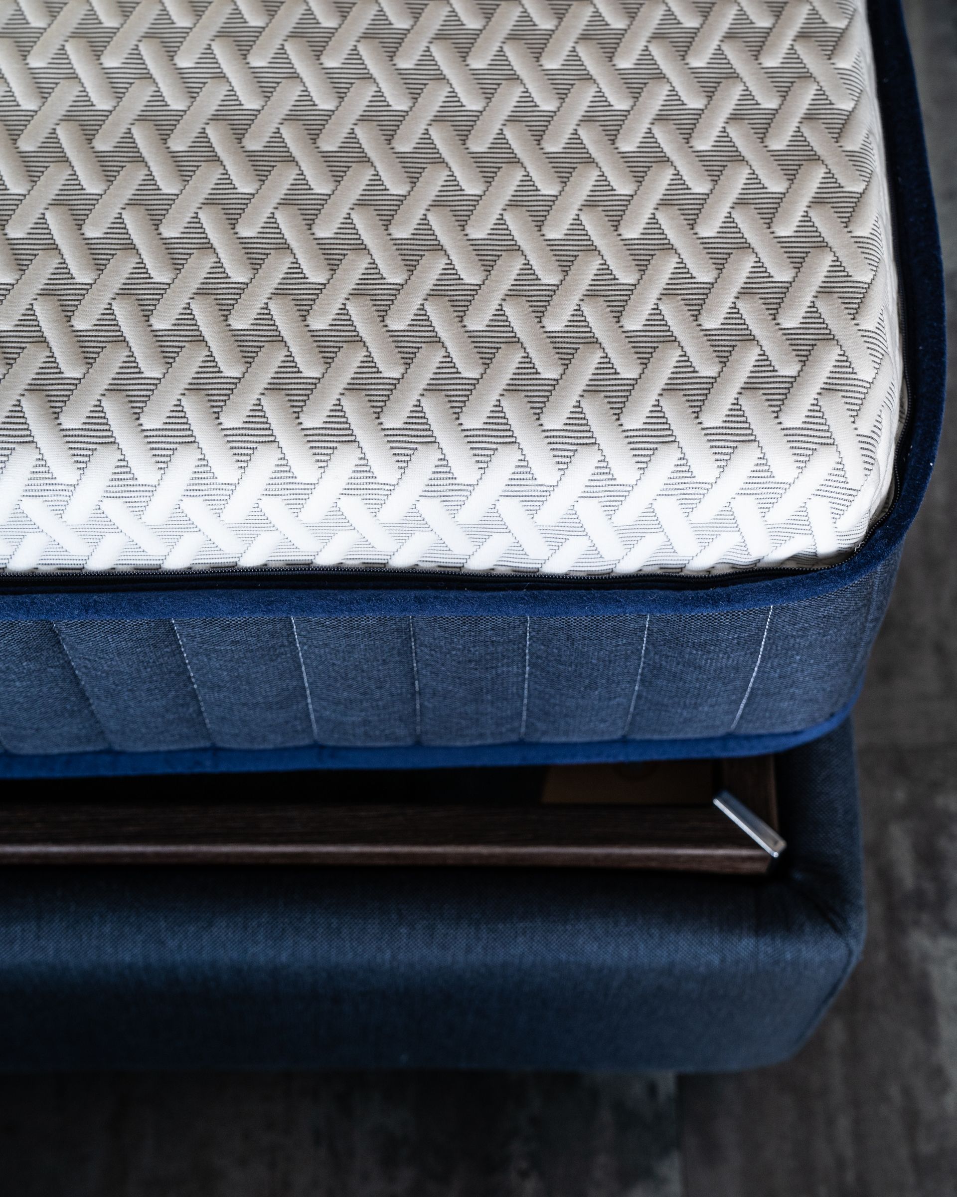 Primo piano di un materasso blu con la parte superiore bianca decorata. Anche la struttura del letto è blu.