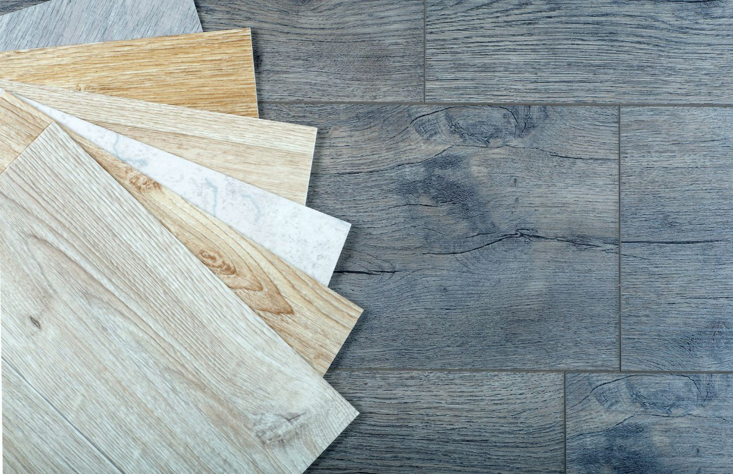 Floor samples fanned out over a gray, patterned floor. Variety of wood tones.