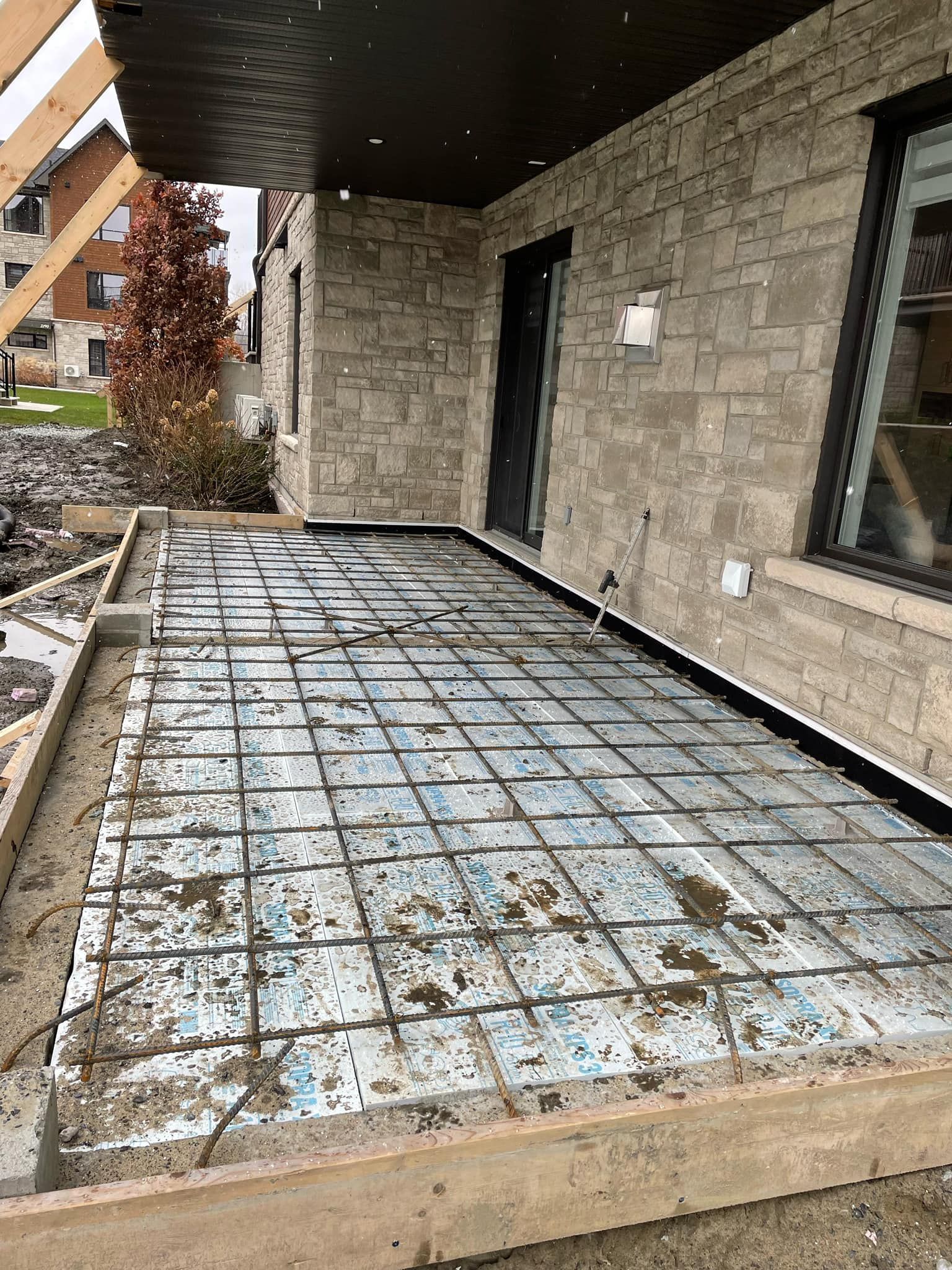 Un patio en béton est en cours de construction devant une maison en briques.