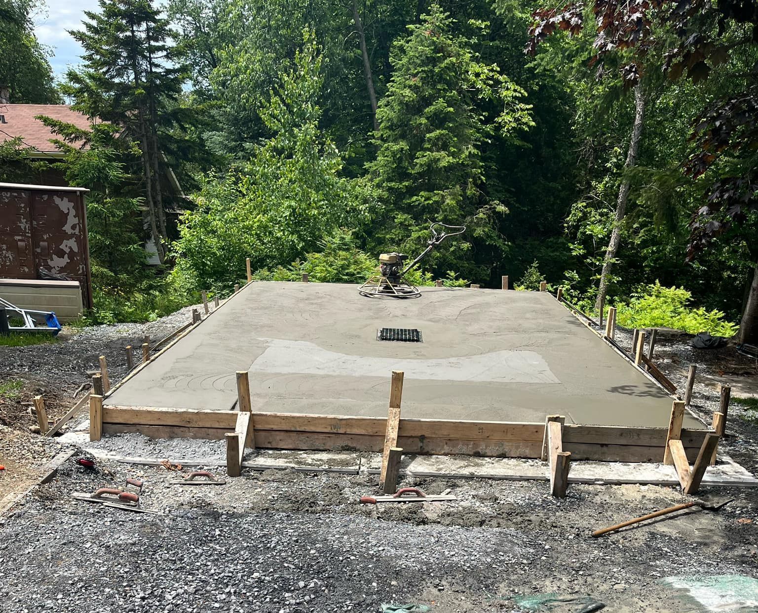 Une dalle de béton est en cours de construction dans une cour arrière avec des arbres en arrière-plan