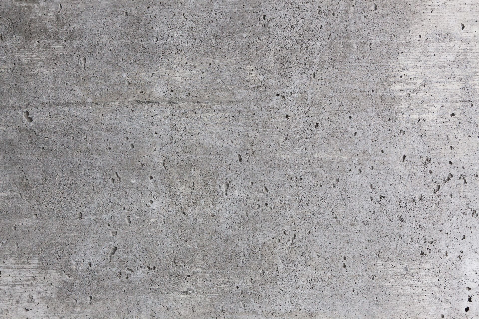 Surface en béton gris, texturée avec de petites piqûres et des lignes horizontales.