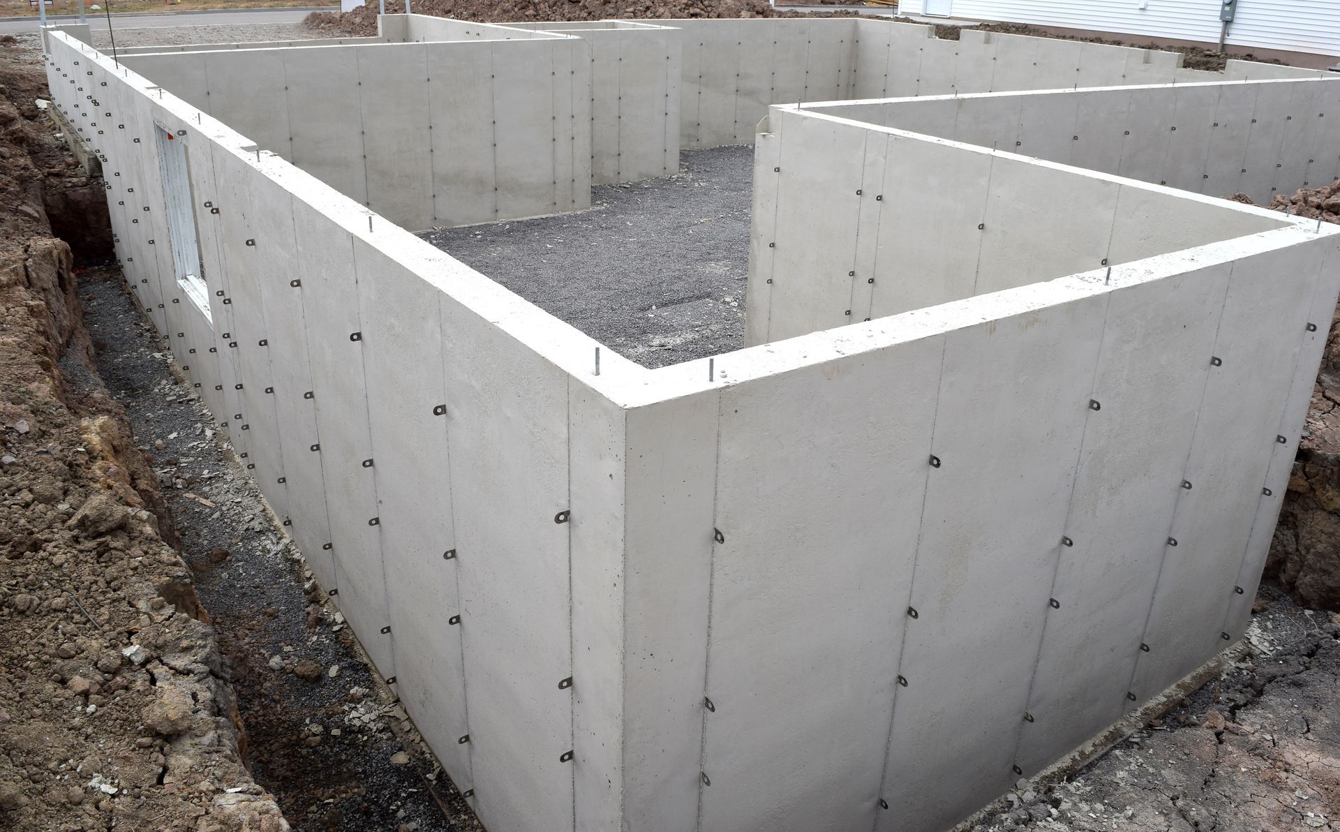Fondations en béton d'un bâtiment en construction, avec base de gravier et fixations métalliques encastrées.