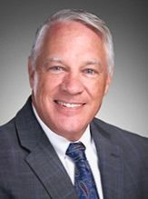 Smiling man in a gray suit and blue tie against a neutral studio background