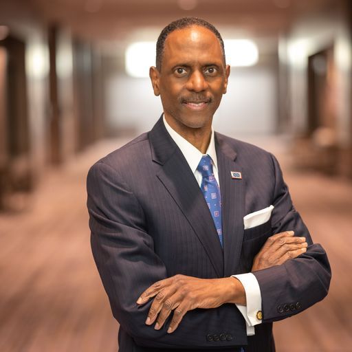 Professional man in a dark suit standing with arms crossed in a softly lit hallway