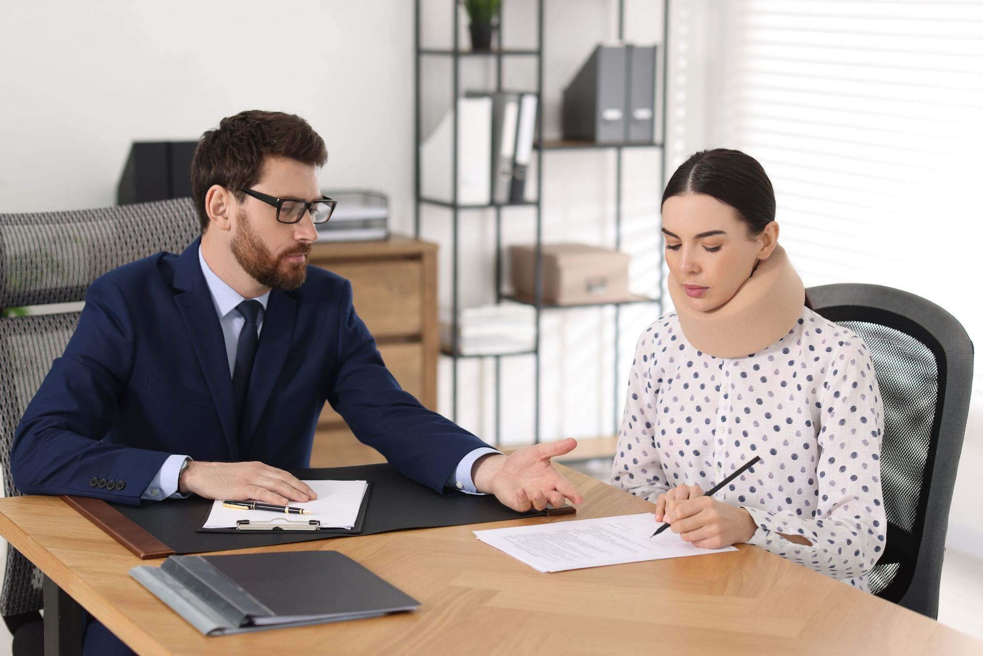 A male lawyer talks to an injured woman signing a document in the lawyer's office. A male lawyer talks to an injured woman signing a document in the lawyer's office.