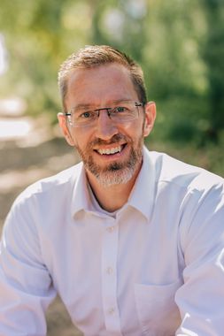 Man wearing glasses and a white shirt smiling outdoors in soft sunlight