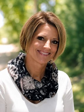 Smiling woman in a white top and patterned scarf outdoors with a blurred green background