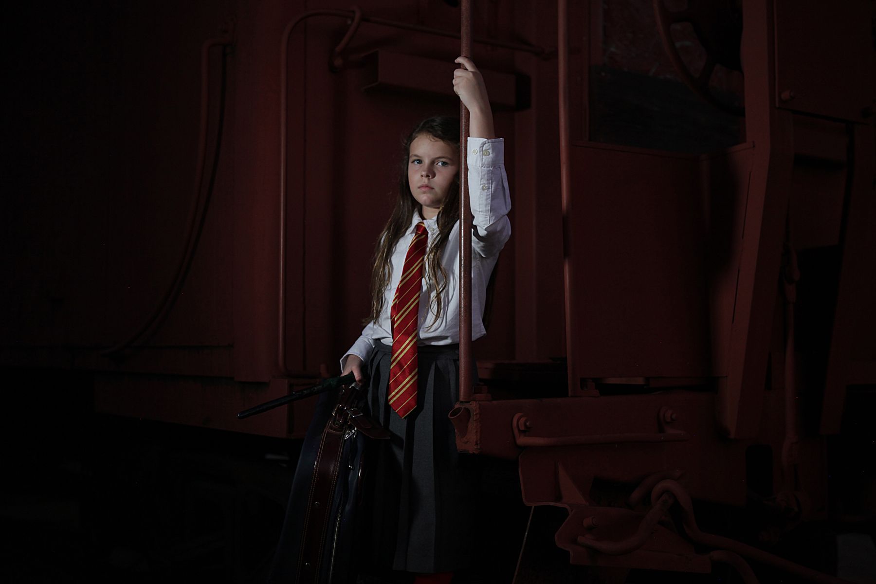 A young girl in a harry potter costume is holding an umbrella in a dark room.