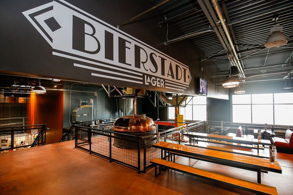Indoor Bierstadt lager hall with long tables, large wall sign, and metal brewing tank