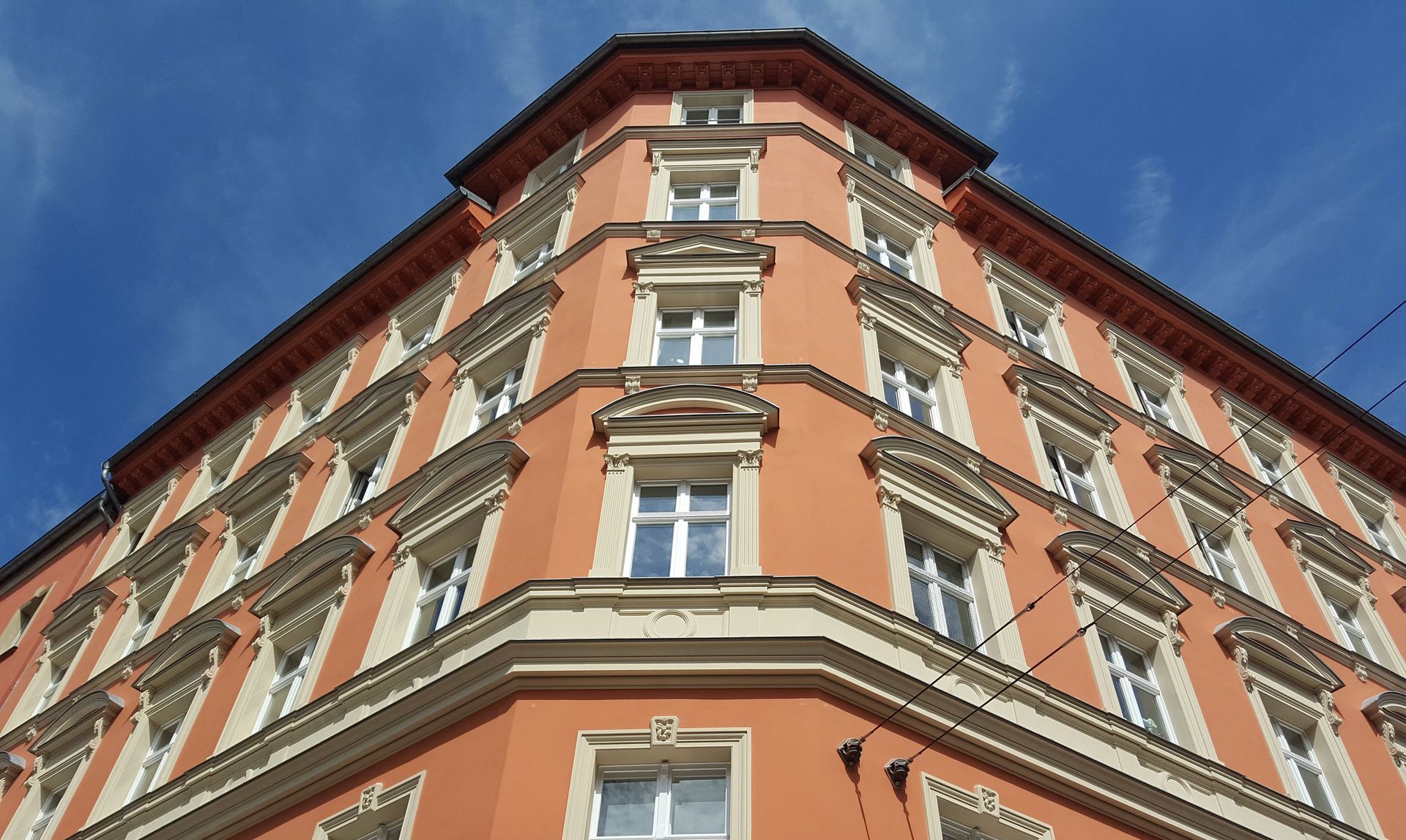 Veduta dal basso di un edificio a più piani color salmone con finiture bianche, sullo sfondo di un cielo azzurro brillante.