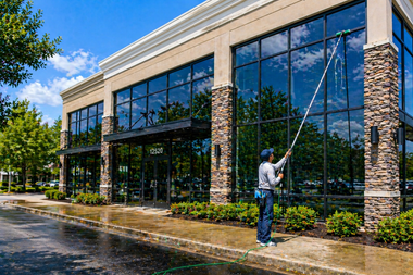 Person washing windows on a modern glass office building with stone columns outside