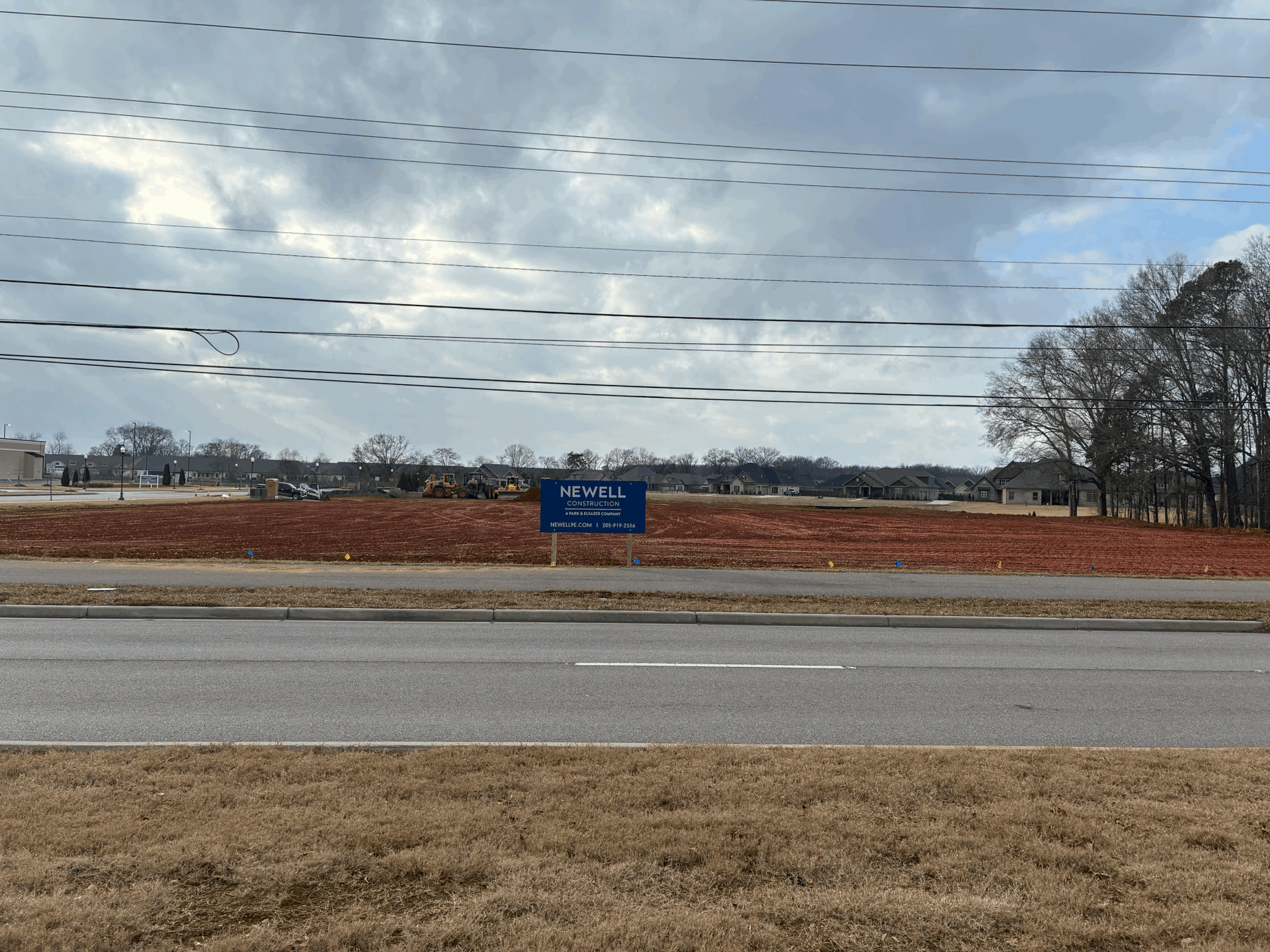Construction site with a sign in front of a cloudy sky and power lines.