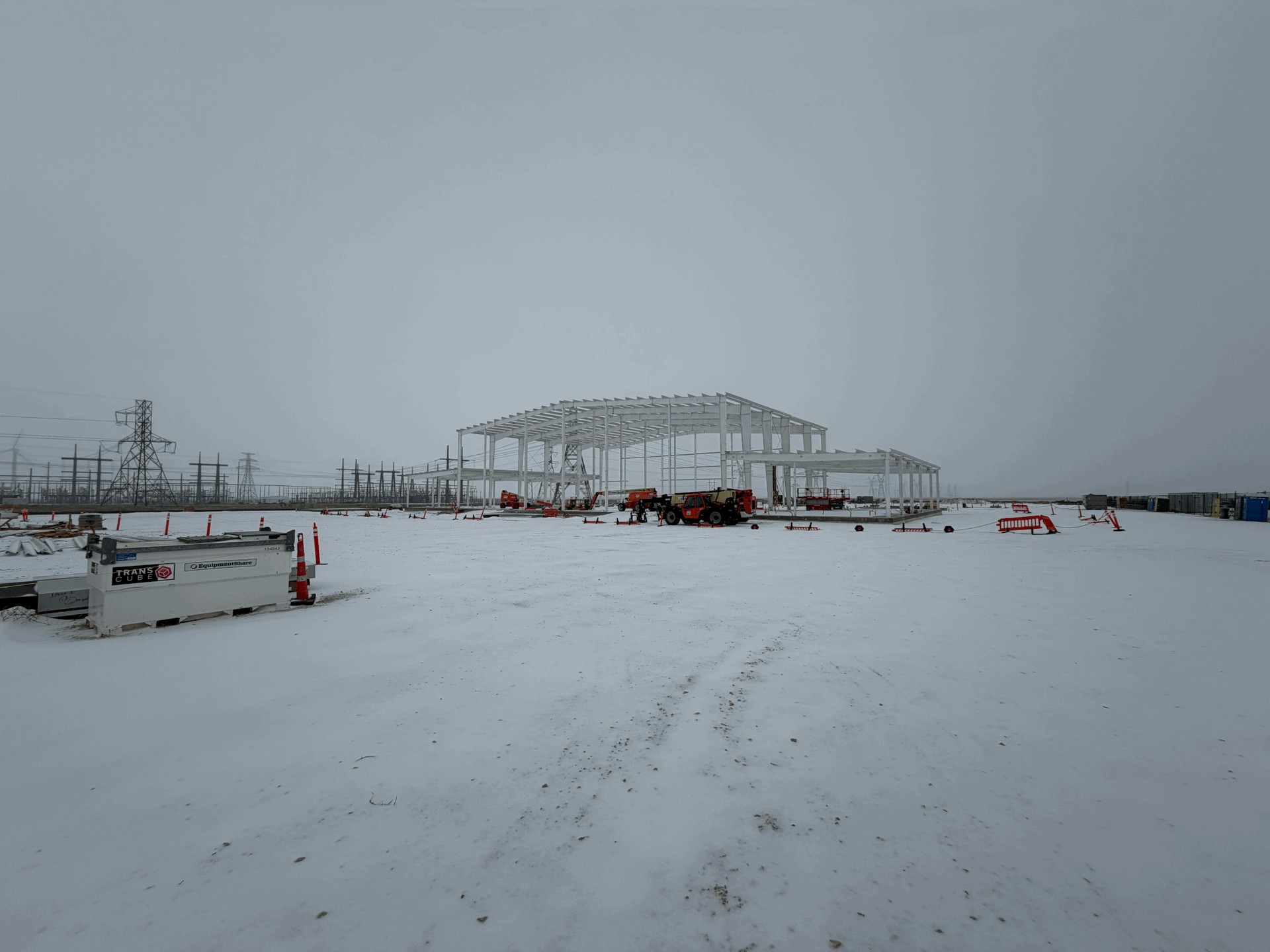 Steel framework of a building under construction in a snowy field on an overcast day.