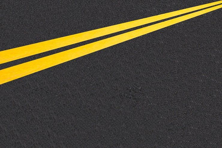 A close-up view of dark asphalt road surface with two parallel yellow painted lane divider lines.