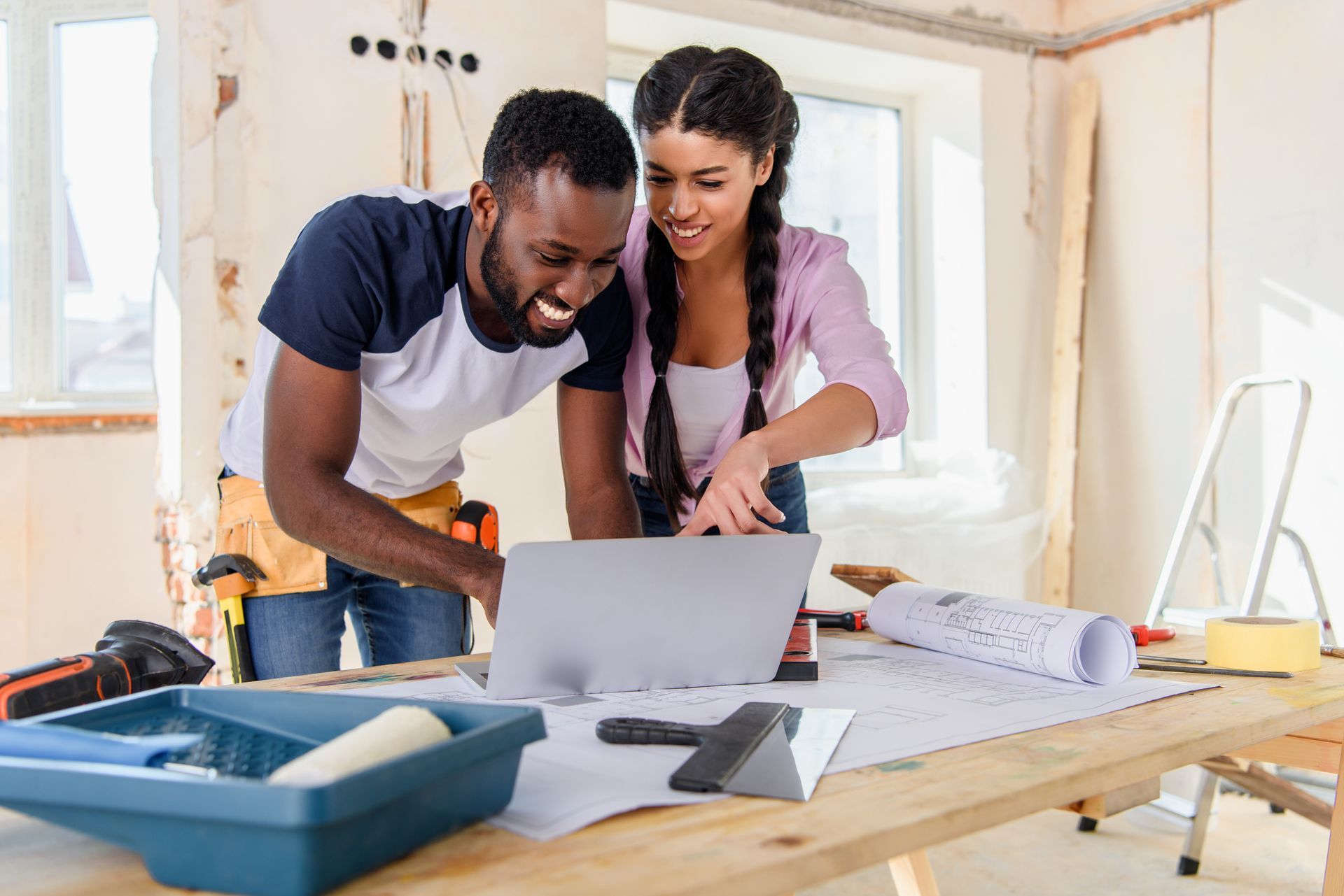 A couple is looking at a laptop in a house that is under renovation.