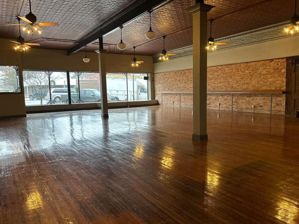 A large empty room with wooden floors and ceiling fans.