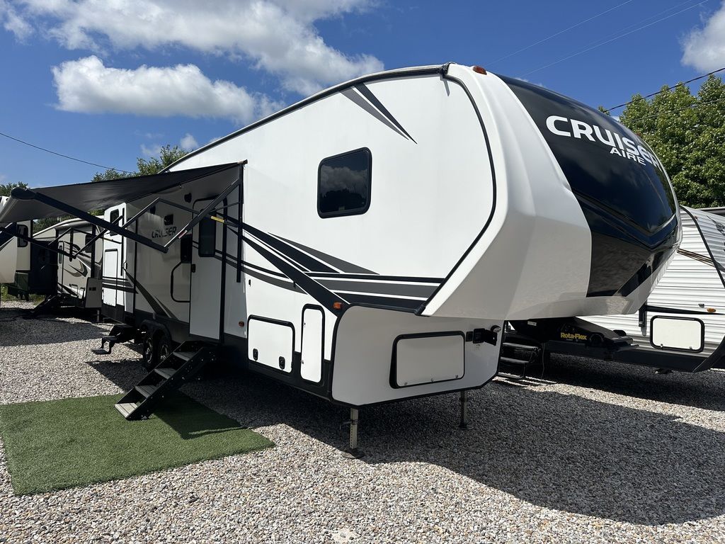 White and black fifth wheel RV parked on gravel with awning extended.