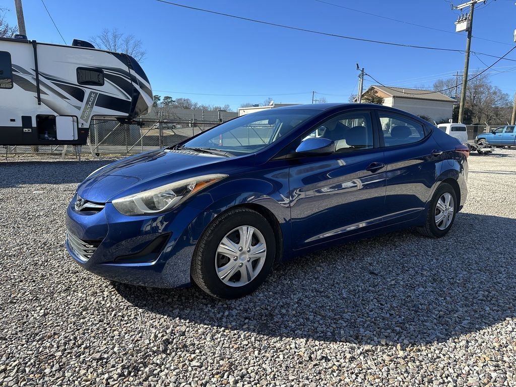 Blue Hyundai Elantra parked on gravel in front of a trailer on a sunny day.